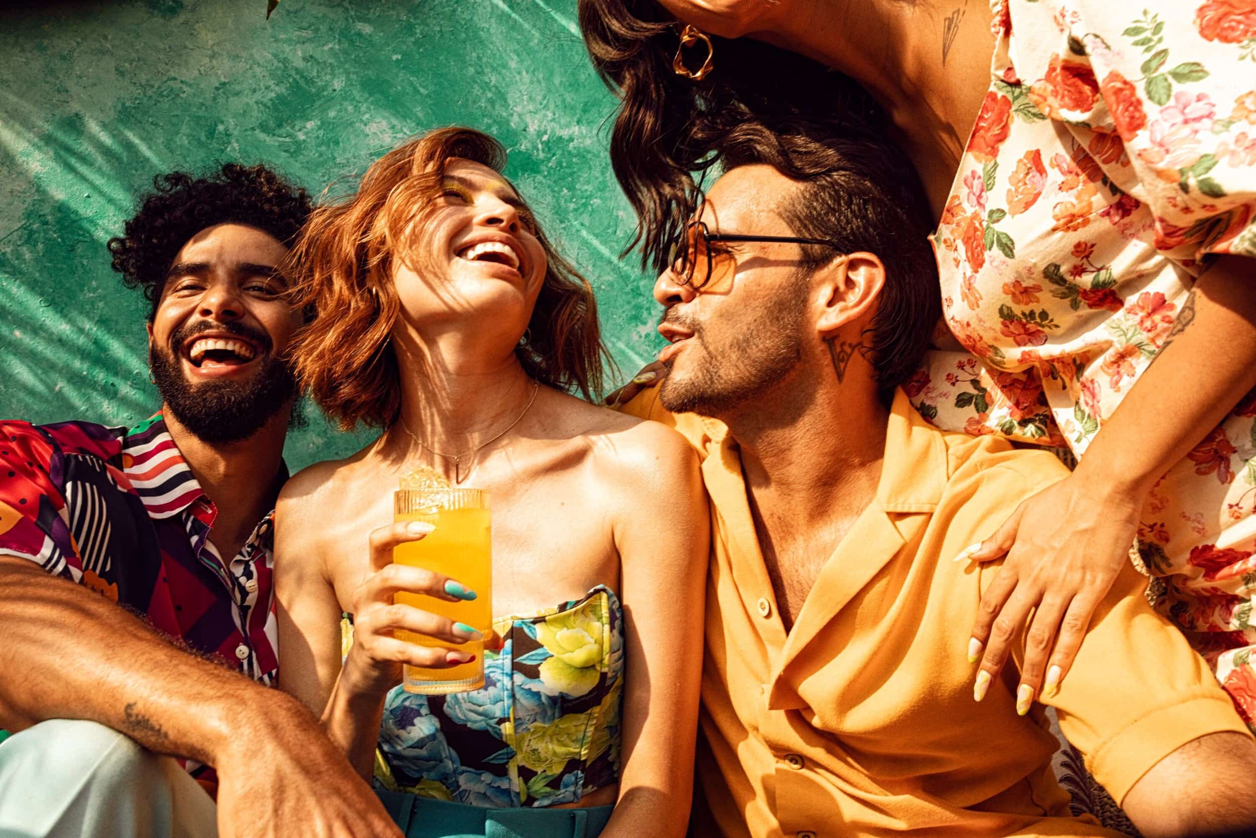 Four people socializing outdoors, laughing together with a cocktail glass in hand.
