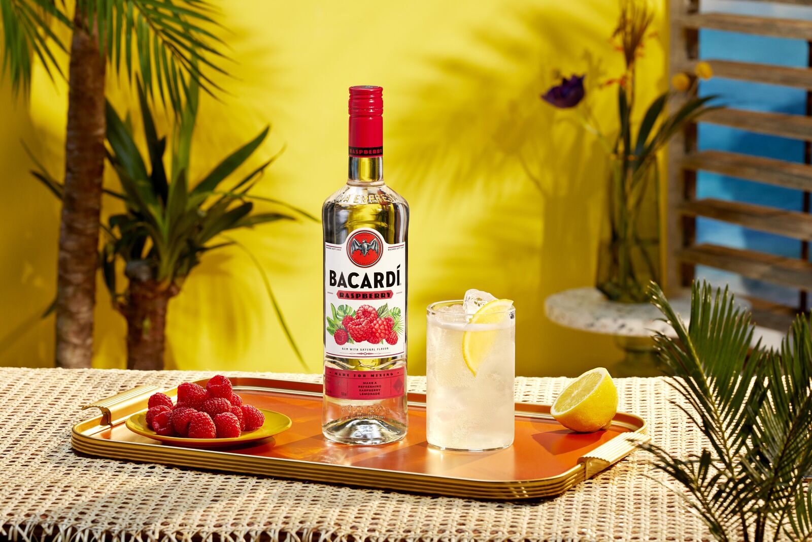 BACARDÍ Raspberry rum bottle next to a cocktail with lemon slice, raspberries, and ice.