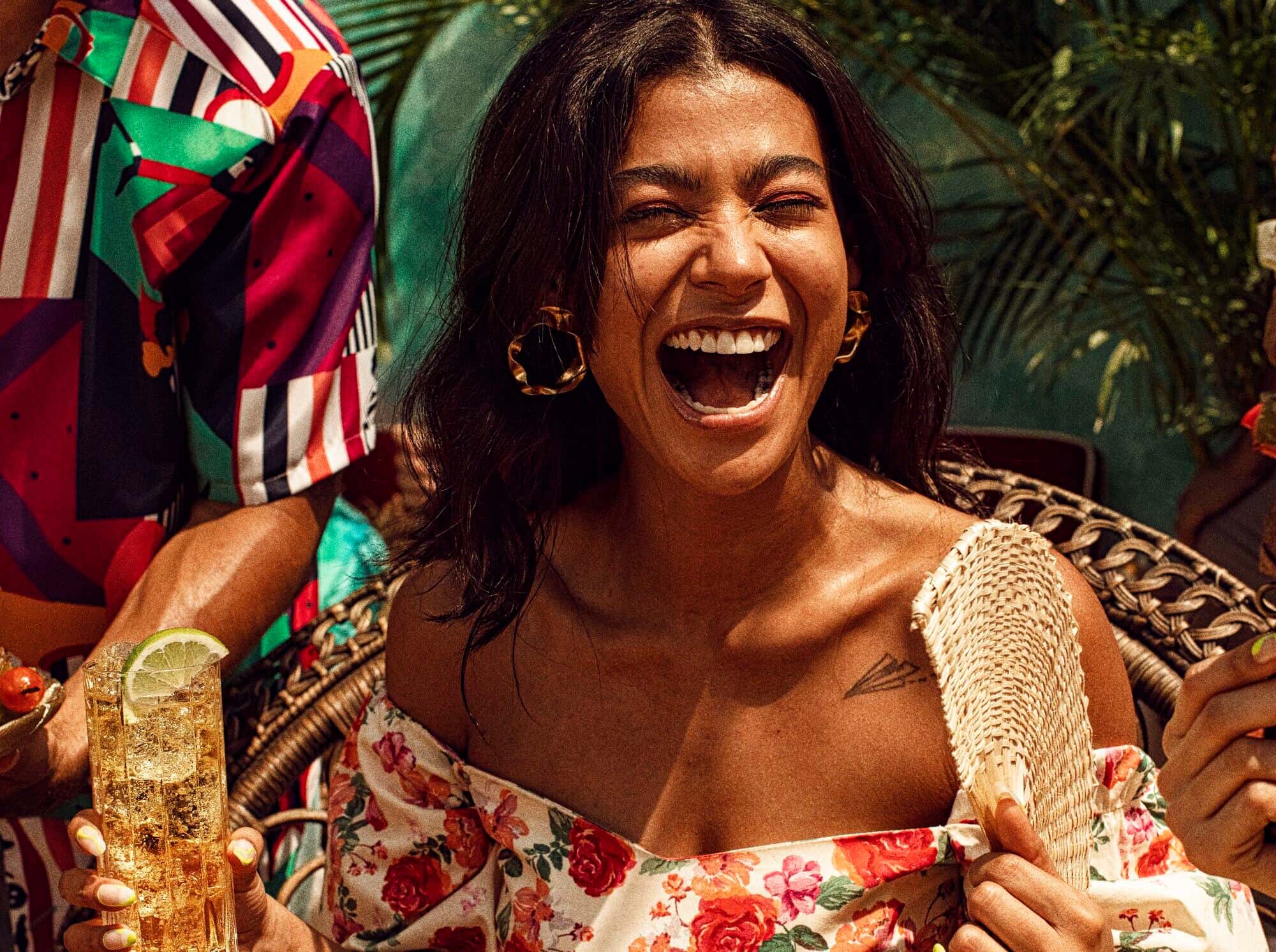 Person laughing while holding a cocktail glass with a lime wedge and woven fan.