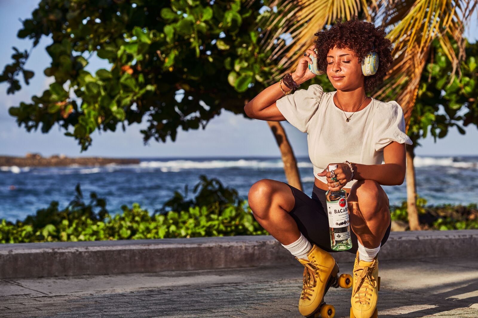 Person holding BACARDÍ bottle while wearing headphones, roller skates.