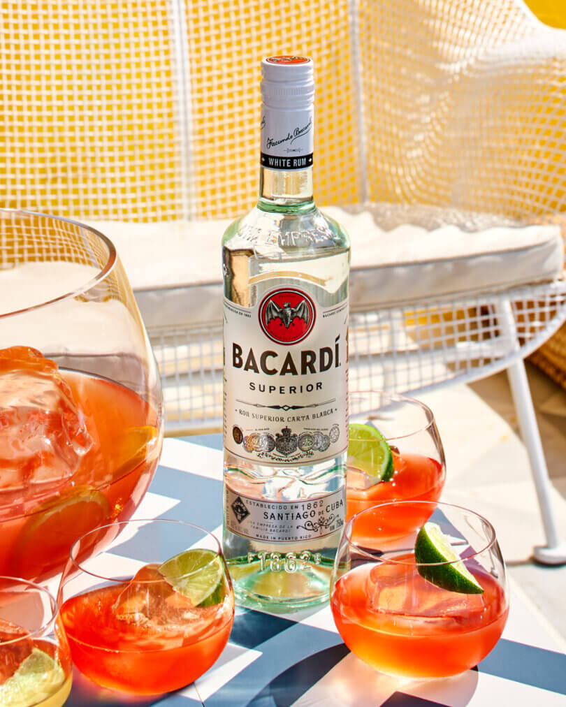 BACARDÍ Superior White Rum bottle with cocktail glasses and a pitcher of orange-red cocktails.