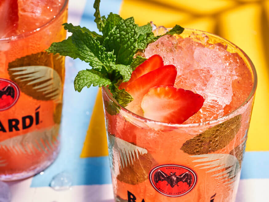 Two cocktail glasses with red drink, mint leaves, strawberries, crushed ice, BACARDÍ logo visible.