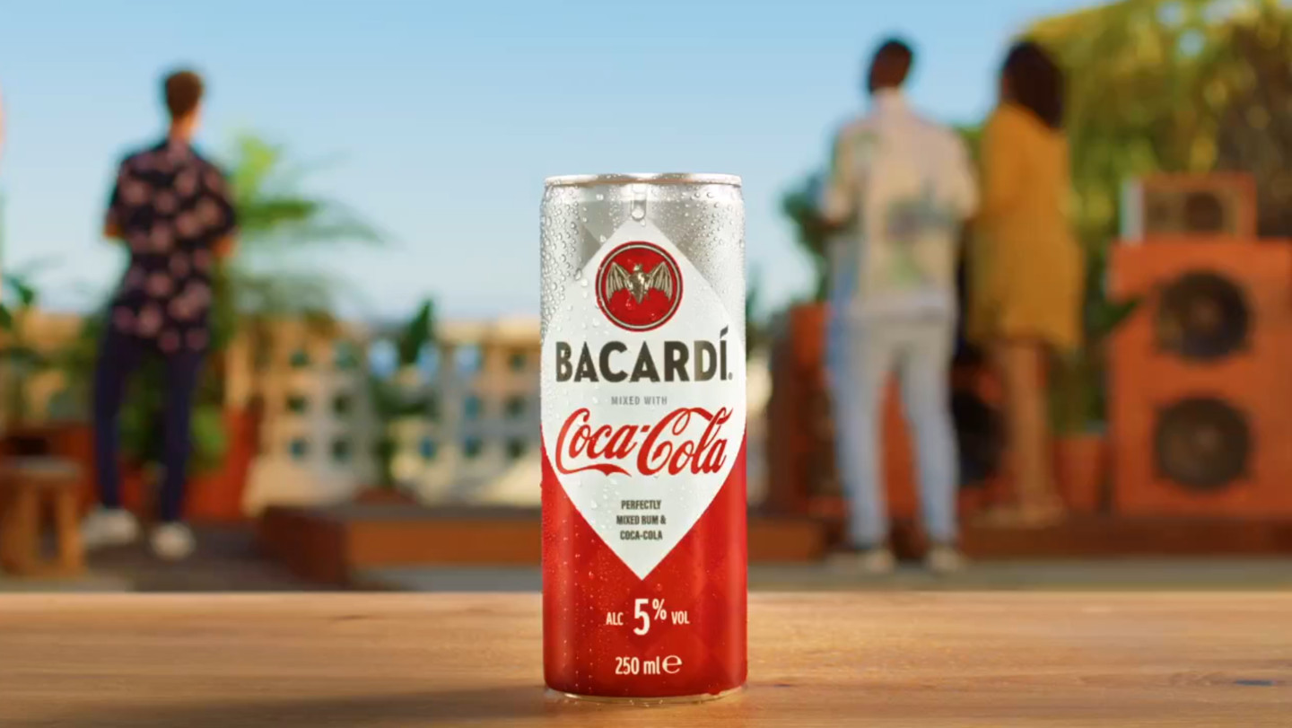 Chilled Bacardí and Coca-Cola can with condensation, positioned in a lively outdoor setting.